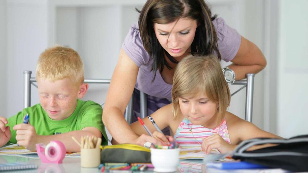 Mère qui aide ses deux enfants souriants à faire les devoirs.