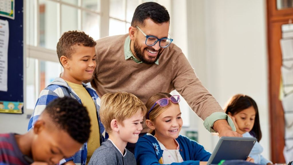Des enfants et un professeur à l'école avec une tablette en classe.