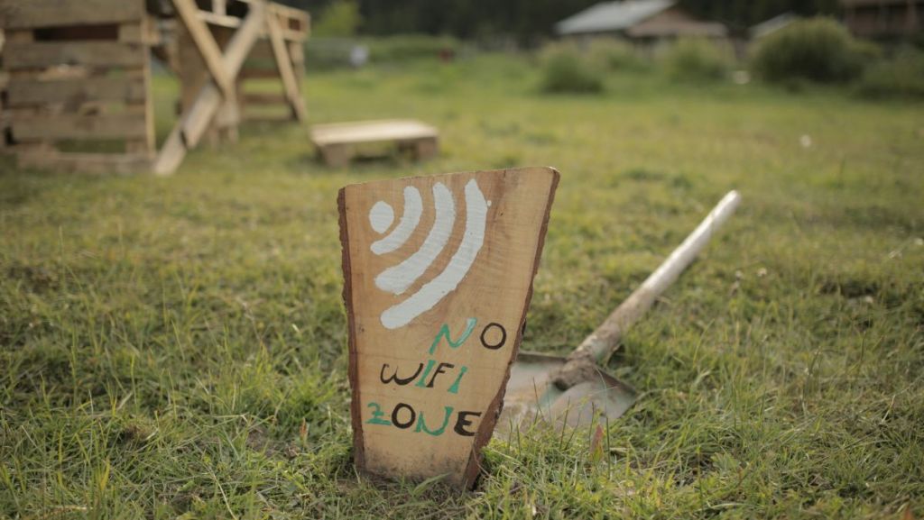 Une pancarte no wifi dans un jardin. Derrière, une pelle posée sur l'herbe. Dans le flou, au loin, une chaise en bois