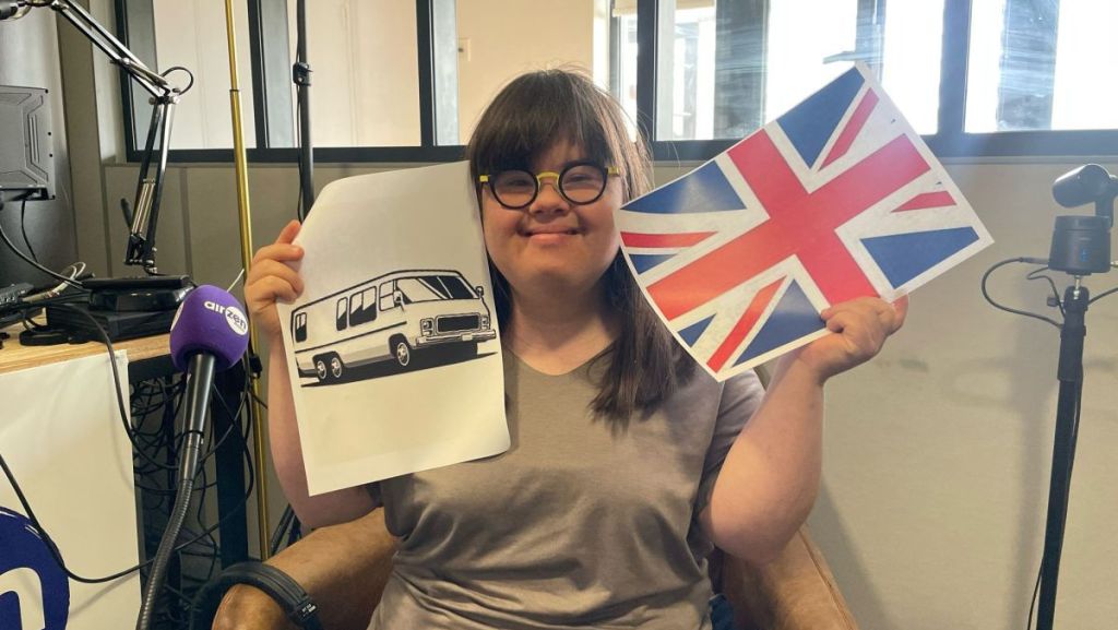 Jeanne avec un drapeau anglais dans la main droite et une image de camping-car dans la main gauche.