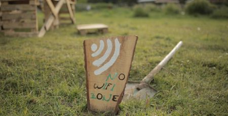 Une pancarte no wifi dans un jardin. Derrière, une pelle posée sur l'herbe. Dans le flou, au loin, une chaise en bois