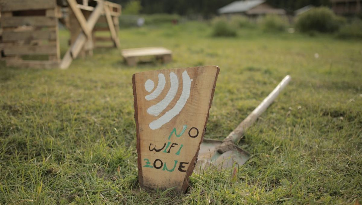 Une pancarte no wifi dans un jardin. Derrière, une pelle posée sur l'herbe. Dans le flou, au loin, une chaise en bois