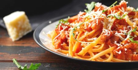 Assiette de pâtes à la sauce tomate avec un morceau de parmesan à côté