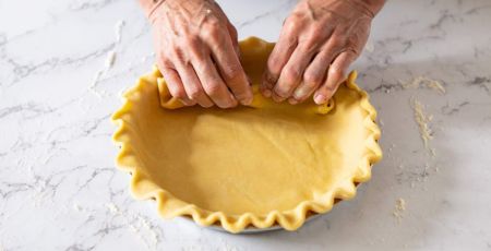 Mains en train de foncer un moule avec une pâte à tarte