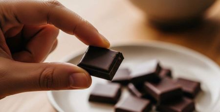 Main qui prend un carré de chocolat noir dans une assiette