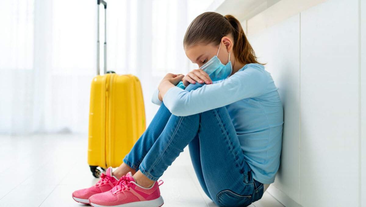 Jeune femme avec un masque à côté de sa valise
