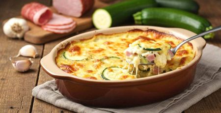Gratind e courgettes crémeux au jambon avec une cuillère qui en prend une part alors que le fromage file.