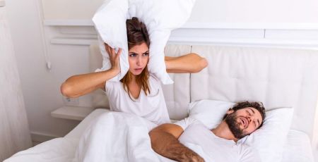 Femme qui se bouche les oreilles au lit à côté d'un homme qui ronfle