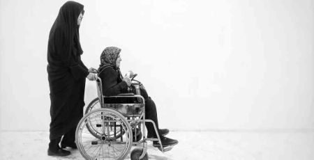 personne âgée en chaise roulante poussée par une femme