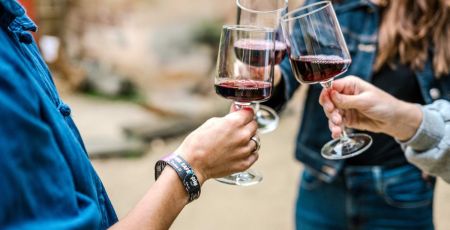 Trois amis trinquent au vin rouge. En premier plan, un bracelet "DRINK SAFE" rappelle l’importance de consommer avec modération, même en plein moment festif.
